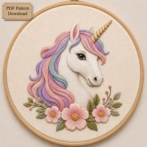 May include: An embroidery hoop containing a fabric piece with a stitched unicorn head featuring a gold horn and a mane of pink, purple, and blue threads. Below the unicorn are pink flowers and green leaves. The text reads PDF Pattern Download.