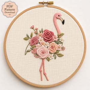 May include: An embroidery hoop containing a fabric piece with a stitched flamingo design. The flamingo's body is composed of various pink and peach-colored roses and small flowers, with green leaves, a pink neck, and two thin pink legs.