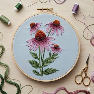 May include: A completed embroidery project featuring a floral design of pink coneflowers with orange centers and green leaves. The embroidery is set in a wooden hoop against a light blue fabric. Spools of thread and gold scissors surround the hoop.