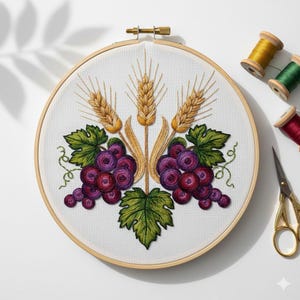 Op de afbeelding: Geborduurd kunstwerk in een houten ring met tarwe en druiven. De tarwe is goudkleurig en de druiven zijn paars. Groene bladeren en ranken omringen de druiven. Gouden schaar en garenklosjes op de achtergrond.