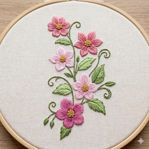 May include: An embroidered floral design featuring pink flowers with yellow centers and green leaves. The embroidery is set in a wooden hoop, showcasing a detailed craft project. The flowers are in varying shades of pink.