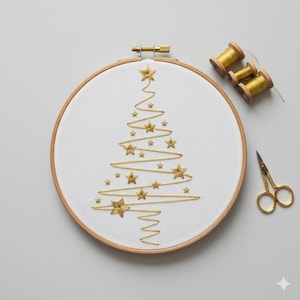 Op de afbeelding: Een gouden geborduurde kerstboom op witte stof, geplaatst in een houten borduurring. De boom is versierd met gouden sterren. Gouden garenklosjes en een kleine gouden schaar liggen in de buurt, wat wijst op een knutselproject.