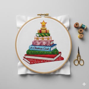 May include: An embroidery hoop features a Christmas tree design made of stacked books. The books are red, green, blue, pink, and gold, with a gold star on top. The text "A Christmas Card" is on one book.