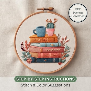 May include: An embroidery hoop containing a stitched design of a stack of four books, a blue mug, and a potted cactus. The books are orange, light blue, pink, and dark blue. Decorative foliage surrounds the stack. Text reads PDF Pattern Download.