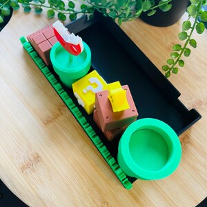 May include: A collection of colorful, themed decorative items. Includes a red and white mushroom, a green pipe, a yellow question mark block, and brown brick blocks. The items are arranged on a wooden surface.