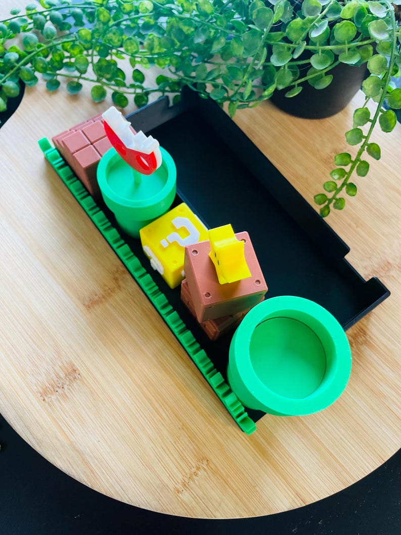 May include: A collection of colorful, themed decorative items. Includes a red and white mushroom, a green pipe, a yellow question mark block, and brown brick blocks. The items are arranged on a wooden surface.