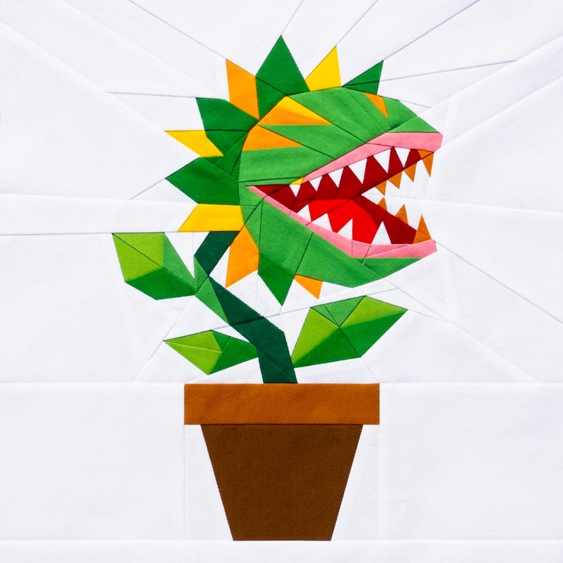 May include: A fabric quilt block featuring a stylized carnivorous plant with green and yellow leaves, a red mouth, and white teeth, set in a brown pot against a white background. The design is constructed from geometric fabric pieces.