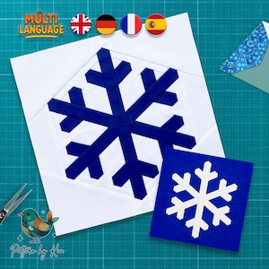 May include: A square quilt block featuring a dark blue snowflake design on a white background, accompanied by a smaller square block showing a white snowflake on a dark blue background. The text MULTI LANGUAGE is visible at the top left.