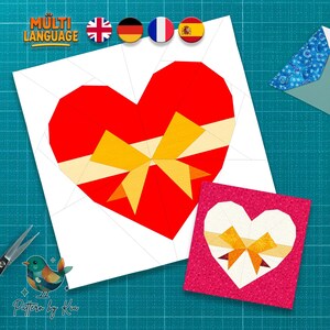 May include: A papercraft design featuring a large red heart with a yellow bow, and a smaller pink square with a white heart and yellow bow. The design is on a white background with the text "MULTI LANGUAGE" and flags.