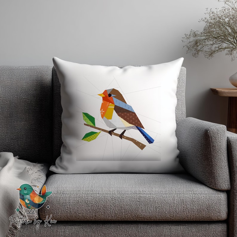 May include: White square throw pillow featuring a geometric design of a bird perched on a branch. The bird has a brown, orange, and blue color scheme. The pillow is on a gray couch.