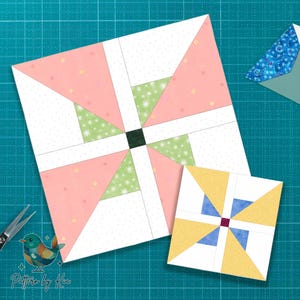 Könnte beinhalten: Zwei farbenfrohe Quiltblöcke auf einer grünen Schneidematte. Der größere Block zeigt rosa, grüne und weiße geometrische Formen. Der kleinere Block hat gelbe und blaue Dreiecke. Eine Schere und ein Logo befinden sich im Bild.