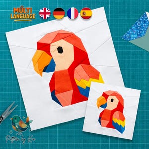 May include: Two white fabric squares with a geometric parrot design in red, orange, yellow, blue, and black. The larger square has the text "MULTI LANGUAGE" and flags. The smaller square is a miniature version of the parrot. The text "Pattern by Kiu" is at the bottom.