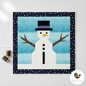 Puede incluir: Un diseño de muñeco de nieve de patchwork con sombrero de copa negro, brazos de ramitas y nariz de zanahoria. El muñeco de nieve está sobre un fondo azul claro y enmarcado por un borde azul marino con estrellas blancas. Un bloque de edredón con temática invernal.