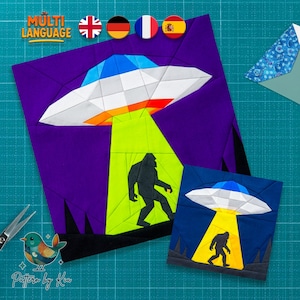 May include: Two fabric art pieces featuring a UFO beaming down on a silhouette of Bigfoot. The larger piece has a purple background, while the smaller one is blue. The text "Multi Language" is at the top.