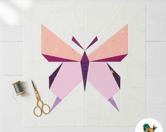 May include: A geometric butterfly quilt block in shades of pink, purple, and peach, set against a white background. Gold scissors and a spool of green thread are on the left. The design is a modern take on a classic quilting pattern.