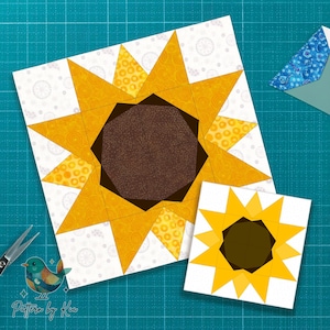 May include: Two sunflower quilt blocks. The larger block features a detailed sunflower design with yellow petals and a brown center. The smaller block is a simplified version. The background is white with a subtle pattern. The image includes scissors and a logo.