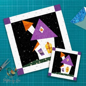 Puede incluir: Dos bloques de edredón con temática de Halloween. El bloque más grande presenta una casa con techo morado, chimenea naranja y una calabaza en el techo. El bloque más pequeño refleja el diseño. Ambos están sobre un fondo negro estrellado y enmarcados en blanco y morado.
