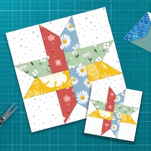 May include: Two star-shaped quilt blocks with floral patterns in red, yellow, green, and blue. The blocks are on a white background with small gray stars. A pair of scissors and a small envelope are also visible.