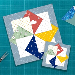 Könnte beinhalten: Zwei farbenfrohe, quadratische Quiltblöcke mit einem Windrad-Design. Der größere Block hat einen hellblauen Rand mit weißen Punkten, und das Windrad hat rote, gelbe, grüne und blaue Abschnitte. Ein kleinerer Block mit dem gleichen Design befindet sich daneben.