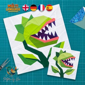 Op de afbeelding: Een quiltpatroon van papier met een grote groene vleesetende plant met scherpe paarse tanden, een roze mond en witte achtergrondsegmenten. Het ontwerp bevat twee formaten van het plantmotief en de tekst Multi Language.