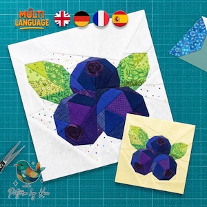Może przedstawiać: Biały kwadrat materiału z patchworkowym wzorem jagód w odcieniach niebieskiego i fioletowego, z zielonymi liśćmi. Obok znajduje się mniejszy, żółty kwadrat z tym samym wzorem. Obraz zawiera tekst "MULTI LANGUAGE".