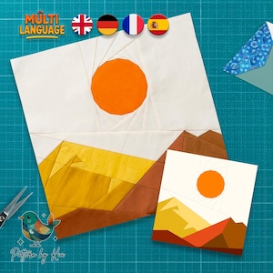 May include: Two fabric art pieces with a landscape design. The larger piece features a white background with a yellow and brown mountain range and an orange sun. The smaller piece has a similar design. The image includes the text "MULTI LANGUAGE" and a logo.