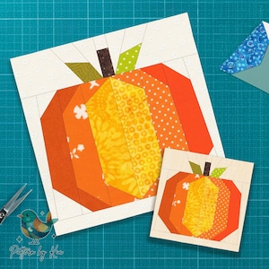 May include: Two paper pieced pumpkin blocks in shades of orange, yellow, and brown. The larger block is approximately 8 inches square, and the smaller one is about 4 inches square. The background is a light cream color.