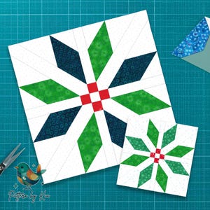 May include: Two white square quilt blocks with a starburst design. The starburst features green and navy blue diamond shapes, with a red square in the center. A smaller version of the design is also present. The background is a teal cutting mat.