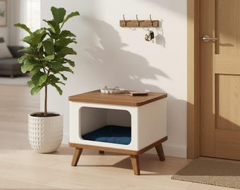 May include: A modern pet house with a white frame, a brown wooden top, and angled wooden legs. The interior features a blue cushion. A potted plant and a key rack are visible in the background.