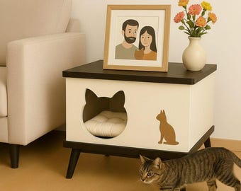 May include: A modern cat house with a black top and white body, featuring a cat-shaped entrance and a brown cat silhouette. A framed portrait and a vase of flowers sit on top. A tabby cat walks in front of the cat house.