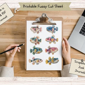 May include: A printable fussy cut sheet on a clipboard featuring eight colorful, illustrated pufferfish in various shades of blue, pink, and yellow. The sheet includes text reading Printable Fussy Cut Sheet, Available in JPG & PDF Format, and Scrapbooking Junk Journals.