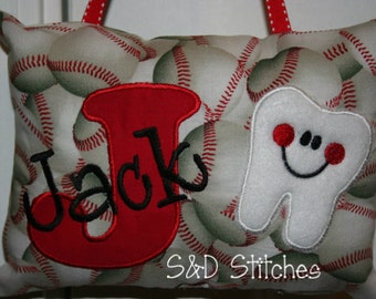 Può includere: Un cuscino rosso e bianco con un motivo a pallone da baseball. Il cuscino ha una grande lettera rossa "J" con cuciture nere e il nome "Jack" cucito in nero. C'è un dente bianco con un viso sorridente e guance rosse cucite sul cuscino. Il cuscino ha il testo "S&D Stitches" cucito sul fondo.