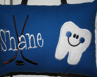 Può includere: Cuscino blu con ricamo bianco del nome "Shane" e due bastoni da hockey. Un dente bianco con un viso sorridente e occhi blu è ricamato sul lato destro del cuscino.