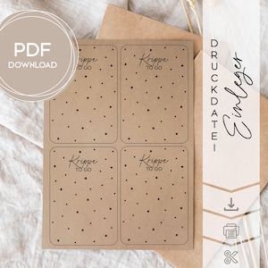 Può includere: Un foglio di quattro etichette rettangolari in carta kraft con angoli arrotondati, ciascuna con una dispersione di piccole stelle nere. Le etichette hanno il testo "Krippe to go" in un carattere scritto a mano. Un'icona di download PDF è in alto a sinistra.