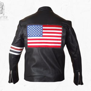 May include: Black leather jacket featuring an American flag patch on the back. The jacket has a classic biker style with a zip-up front, zippered sleeves, and red, white, and blue stripes on the left sleeve. The jacket is a leather specialist product.