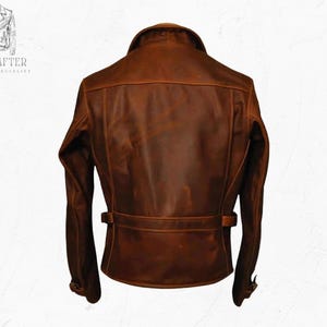 May include: A brown leather jacket with a classic design. The jacket features a collar, shoulder detailing, and a belt around the waist. The back of the jacket is visible, showcasing the stitching and texture of the leather. The jacket has a vintage, worn look.