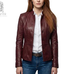 Op de afbeelding: Bordeaux leren jasje met knoopsluiting, gedragen over een wit overhemd met kraag en een blauwe jeans. De jas heeft een getailleerde pasvorm en een opstaande kraag. Het merklogo "MR KRAFTER LEATHER SPECIALIST" staat linksboven.