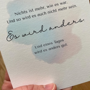 Op de afbeelding: Een witte kaart met Duitse tekst en aquarelaccenten. De tekst luidt: "Nichts ist mehr, wie es war. Und so wird es auch nicht mehr sein. Es wird anders. Und eines Tages wird es anders gut."