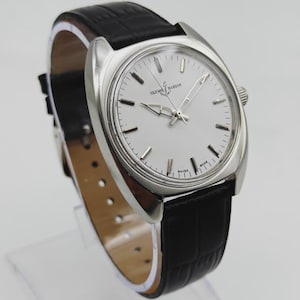 May include: A silver wristwatch with a white face and a black leather strap. The watch face displays the text "ULYSSES NARDIN SWISS MADE". The strap has a crocodile skin pattern.