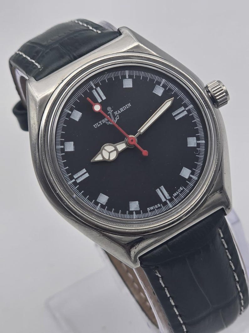 K&ouml;nnte beinhalten: Eine Edelstahl-Armbanduhr mit schwarzem Zifferblatt und schwarzem Lederarmband. Die Uhr hat wei&szlig;e Stundenmarkierungen, einen roten Sekundenzeiger und den Text "ULYSSES NARDIN SWISS MADE". Sie hat eine silberne L&uuml;nette und ein strukturiertes schwarzes Lederarmband.