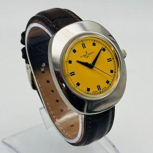 May include: A vintage Ulysse Nardin watch with a bright yellow face and black hour markers. The watch has a silver-tone case and a dark brown leather band. The watch is displayed on a clear stand.