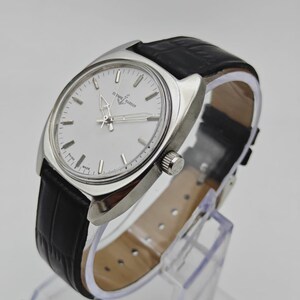 May include: A silver wristwatch with a white face and a black leather strap. The watch has a round face with silver hands and markers. The strap has a crocodile pattern. The watch is displayed on a clear stand.