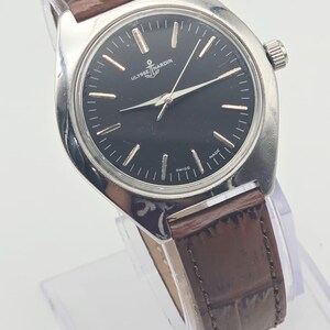 May include: A silver-toned wristwatch with a black face and brown leather band. The watch face features silver hour markers and hands, with the brand name "ULYSSE NARDIN" and an anchor logo. The band is approximately 0.75 inches wide.