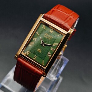 Puede incluir: Un reloj Seiko Quartz dorado con una esfera verde rectangular y n&uacute;meros romanos. El reloj tiene una correa de cuero marr&oacute;n. La esfera del reloj tiene un patr&oacute;n texturizado y el logotipo de Seiko Quartz.