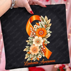 Könnte beinhalten: Ein schwarzer Stoffartikel mit einer orangefarbenen Bewusstseinsschleife, die mit einem Bündel aus orangefarbenen und cremefarbenen Blumen sowie grünen Blättern verziert ist. Der Text "Leukemia Awareness" steht in orangefarbener Schreibschrift unten.