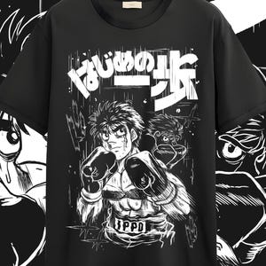 May include: Black t-shirt featuring a manga-style illustration of a boxer in action, wearing boxing gloves and a belt with the word "IPPO". The shirt also has Japanese text in white. The design is a bold, graphic style.