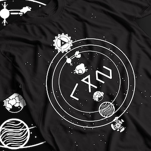 May include: A black t-shirt featuring a white graphic print of a celestial system. The design includes concentric circles, various planets, a sun-like icon with a triangle, and abstract geometric symbols arranged in a circular orbital pattern.