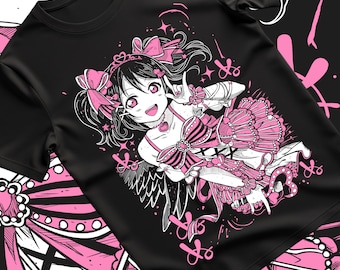 以下が含まれることがあります： 黒いTシャツ。ピンクと白のアニメスタイルのイラストで、髪にリボンをつけた女の子が描かれています。デザインには星、ハート、フリルのドレスが含まれています。シャツは柔らかく快適な素材で作られています。