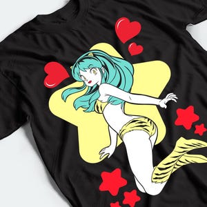 以下が含まれることがあります： 長いティール色の髪をしたアニメキャラクターのグラフィックが描かれた黒いTシャツ。キャラクターは黄色と黒の虎柄のビキニとブーツを着用しています。大きな黄色い星の前に配置され、赤いハートと星に囲まれています。