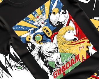 Op de afbeelding: Zwart t-shirt met een kleurrijke anime-stijl illustratie. Het ontwerp toont een robot, een vrouw met blond haar en een man in een groen pak. De tekst "MOBILE SUIT GUNDAM WING" is ook zichtbaar.